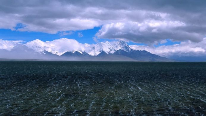 Snowy mountains beyond a vast lake under a cloudy sky