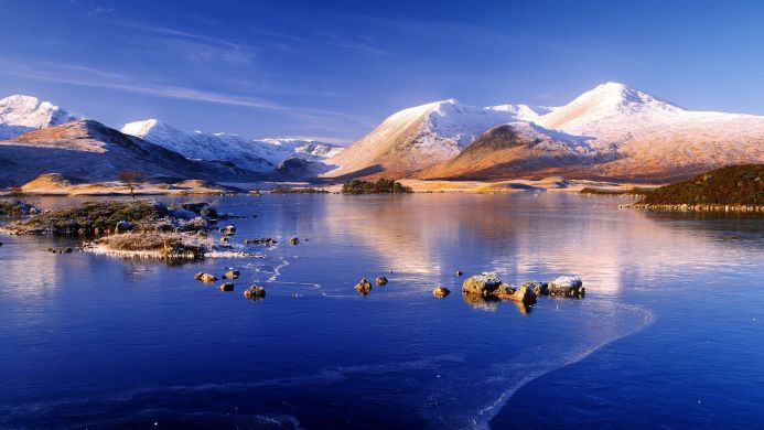 Snowy mountains reflected in a frozen lake under a blue sky