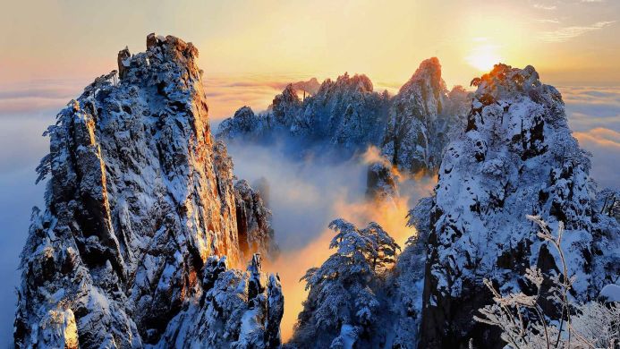Snowy mountain peaks illuminated by the sunrise, with mist filling the valleys