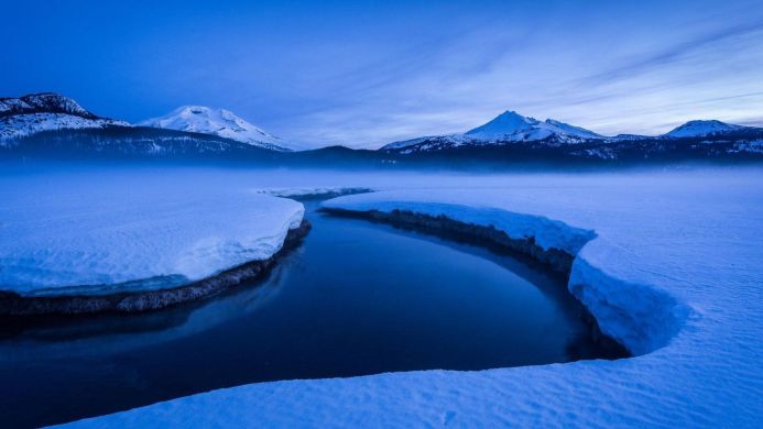 Snowy river landscape with mountains in the background, bathed in blue light