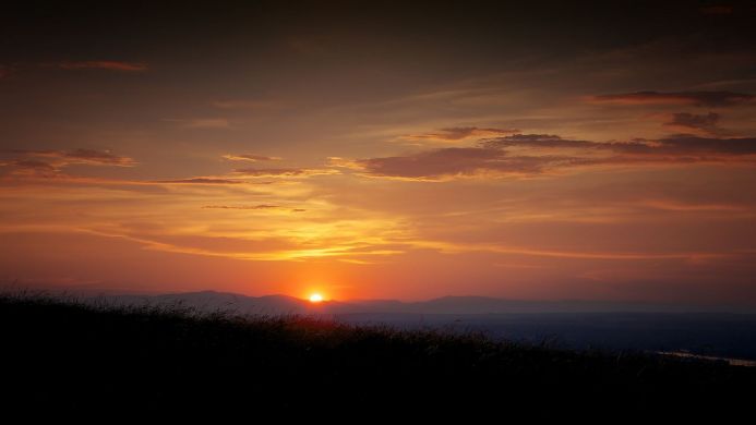 A vibrant sunset over mountains with silhouette of grass in the foreground
