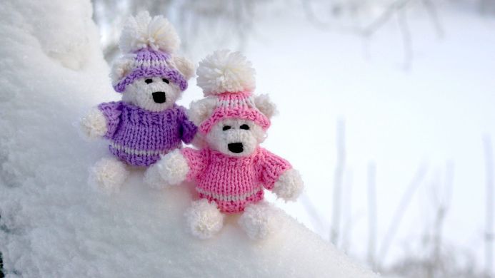 Two teddy bears wearing knit hats and sweaters sitting in the snow