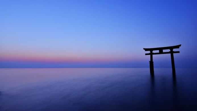 Silhouette of a Torii gate in the water against a blue and purple sky at sunset