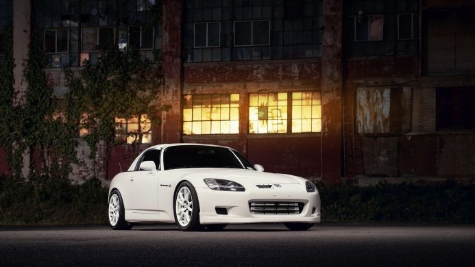White Honda S2000 sports car parked in front of a red brick building with large windows