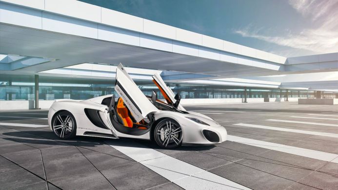 White McLaren MP4-12C with gull-wing doors open under a modern building structure