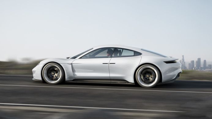 White Porsche Mission E driving on a road with a city skyline in the background