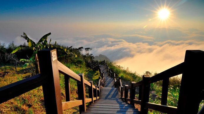 Wooden stairs leading up to the clouds with a bright sun in the background