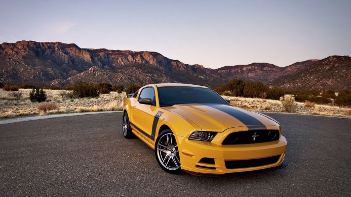 Yellow Ford Mustang Boss 302 parked on a road with mountains in the background
