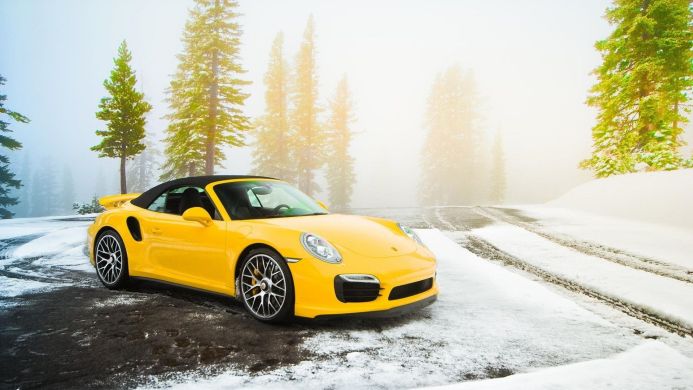 Yellow Porsche 911 Turbo S Cabriolet parked in a snowy forest setting