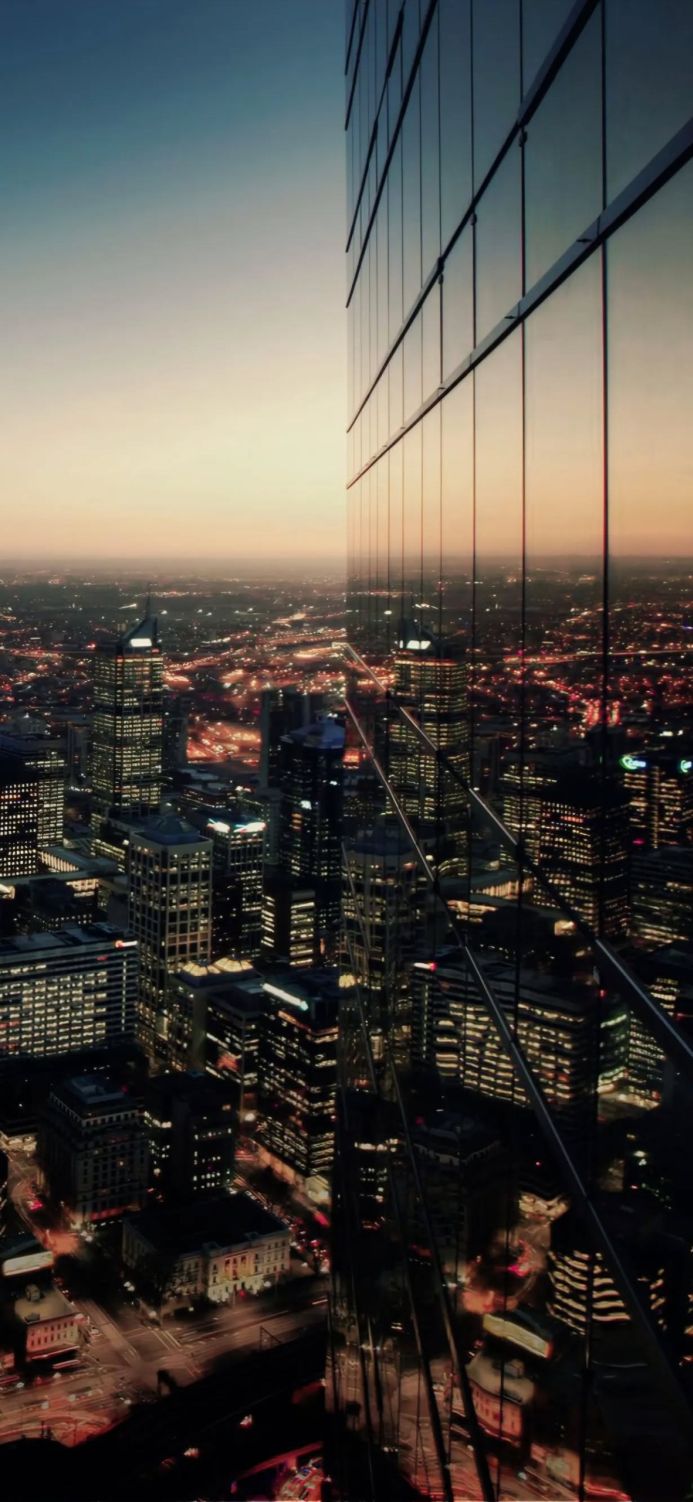 Aerial view of a city at night with illuminated buildings reflected in a skyscraper's glass facade