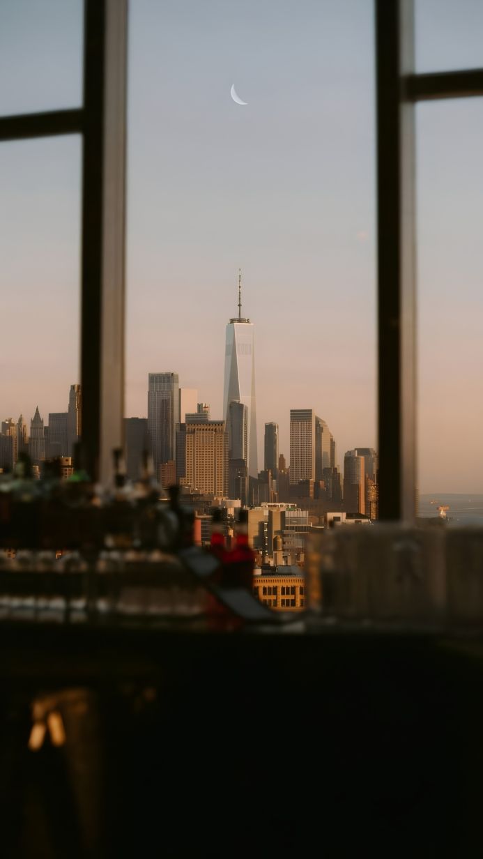 City skyline with skyscrapers under a crescent moon, seen through a window