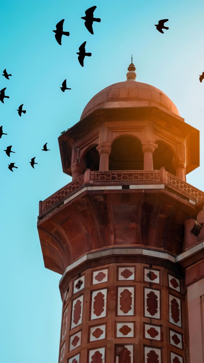 A minaret with flying birds against a light blue sky