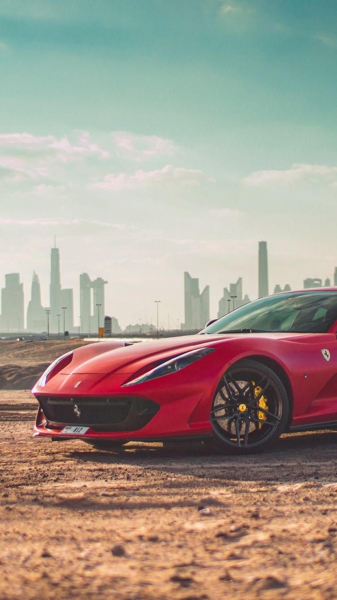 A red Ferrari sports car parked with a city skyline in the background