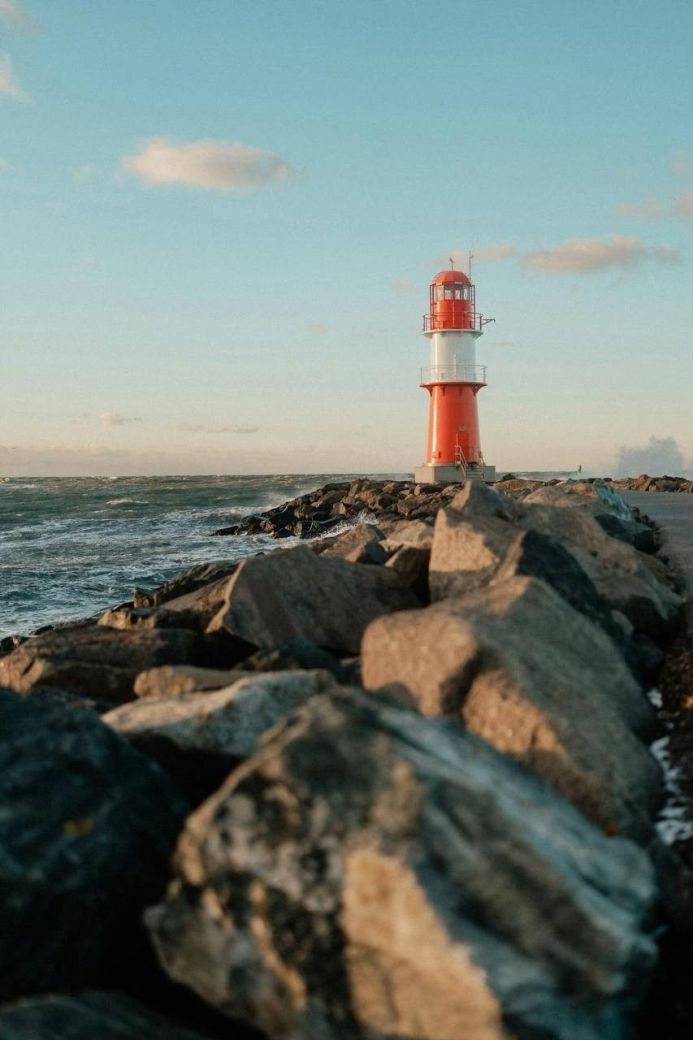 Red and white lighthouse on a rocky coast with ocean waves under a blue sky