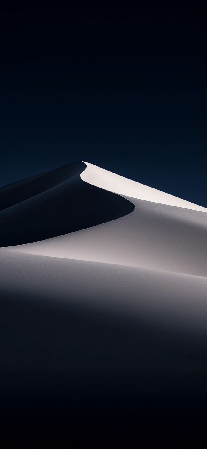 A monochrome image of a sand dune against a dark blue sky