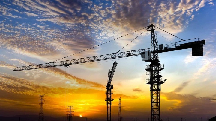 Construction cranes silhouette against a dramatic sunset