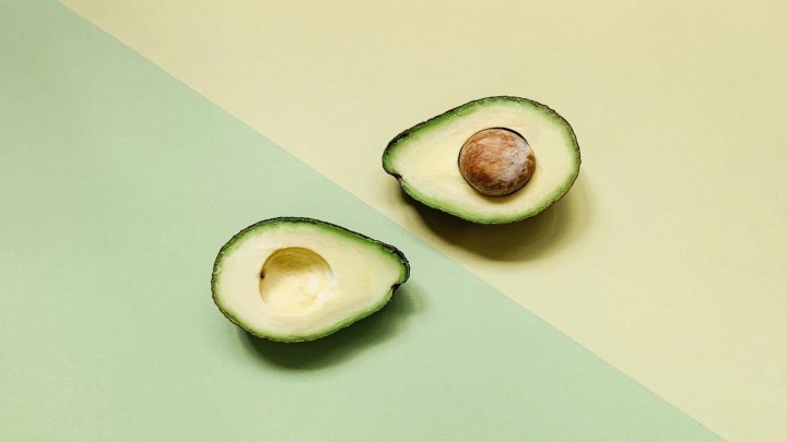 Cut avocado with pit on green background