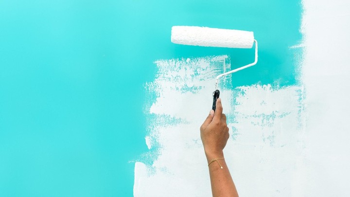 Hand painting wall white with roller on teal background