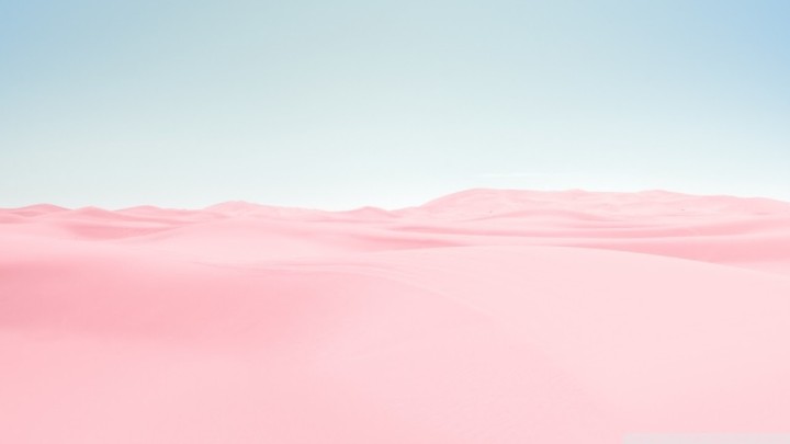 Pink sand dunes under pale blue sky landscape