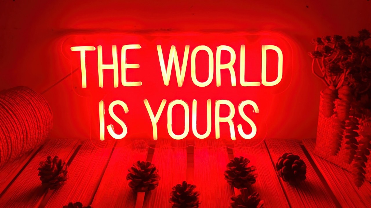 Red neon sign THE WORLD IS YOURS on wood with pine cones