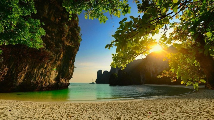 Tropical beach framed by rocks and leaves sunset rays