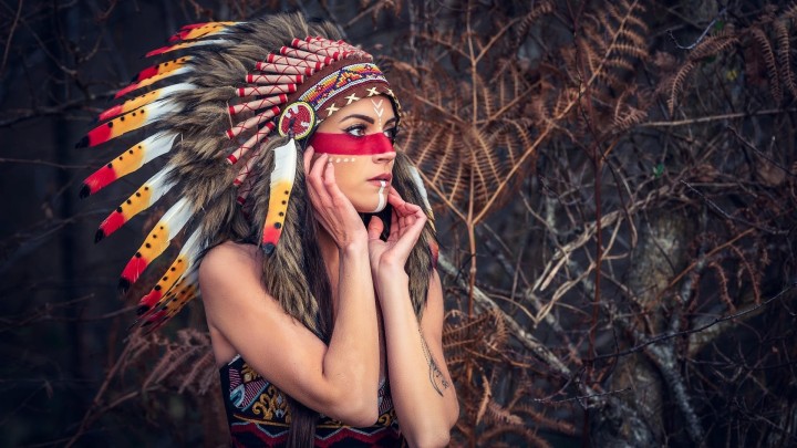 A woman in Native American headdress holds an axe