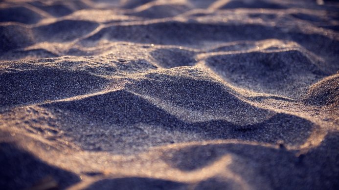 Close-up of dark sand with golden light highlighting the texture