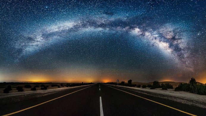A long road through the desert under a starry sky, including the Milky Way