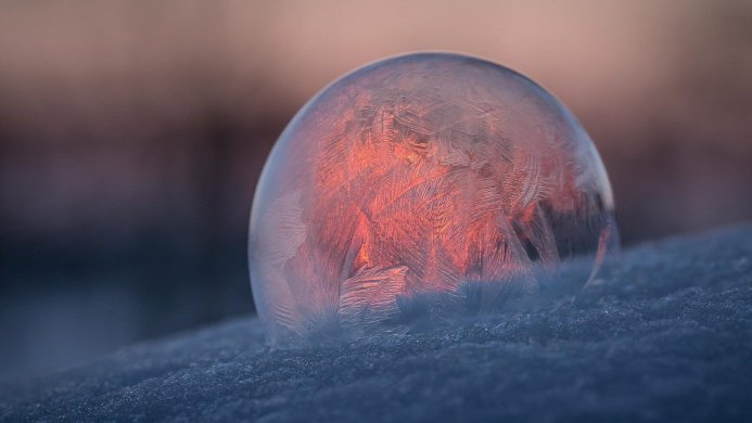 A frozen soap bubble with ice crystals reflecting an orange sunset