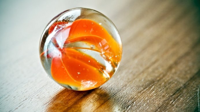 Close-up of a clear glass marble with orange swirls on a wooden surface