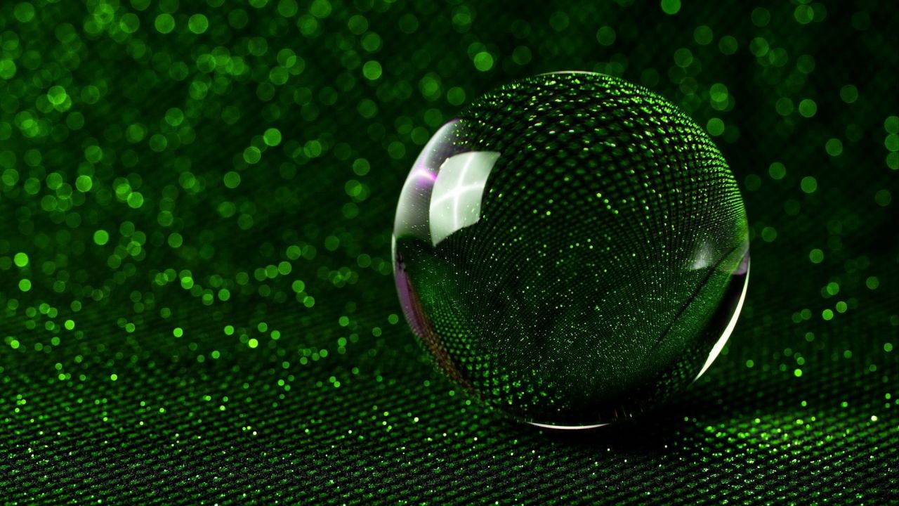 Green glass sphere with bokeh on dark background