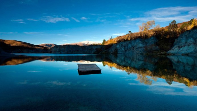 A wooden dock floats on a calm lake reflecting the mountains and sky above