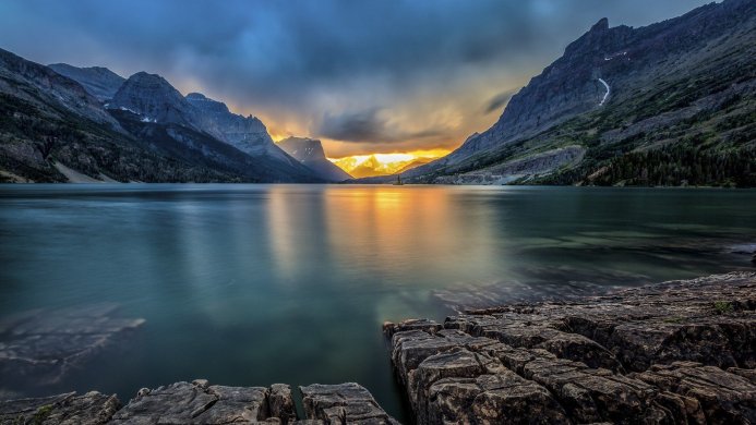 Lake and mountains landscape with sunset reflection on water, rocks in foreground