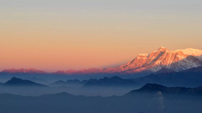 Mountain range with snow-capped peaks at sunrise, shrouded in mist