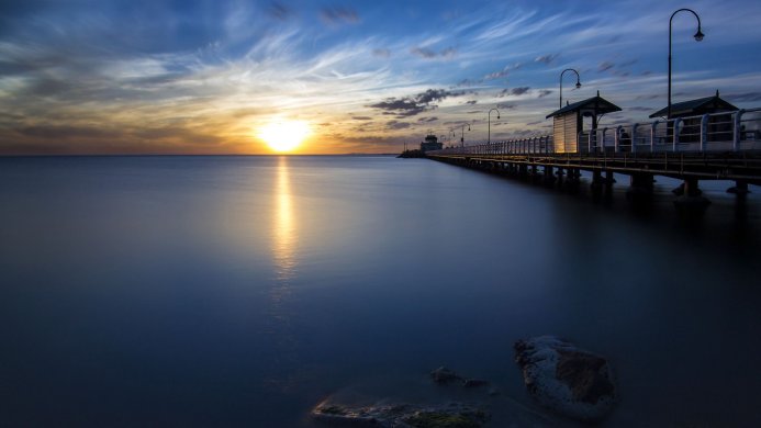 Long pier stretching out into the sea at sunset with vibrant colors in the sky