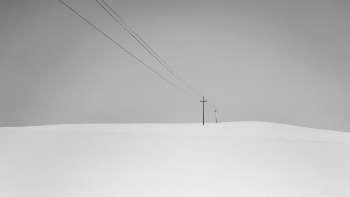 Power lines and utility poles over a snowy hill in a black and white minimalist landscape