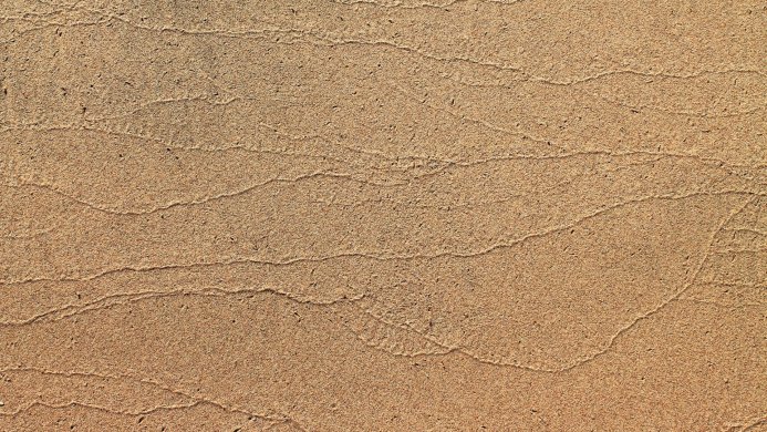 Close-up of sand with wavy lines on a beach, natural texture