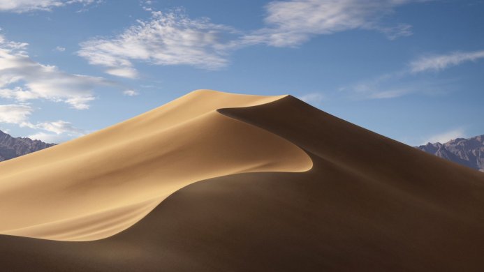 A large sand dune with mountains in the background under a blue sky with wispy clouds