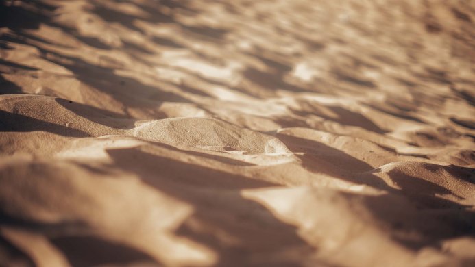 Close up of sand dunes with natural light and shadows, creating a textured surface
