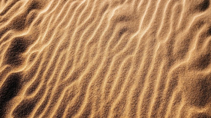 Waves of sand in the desert under the sun, beige and brown texture background