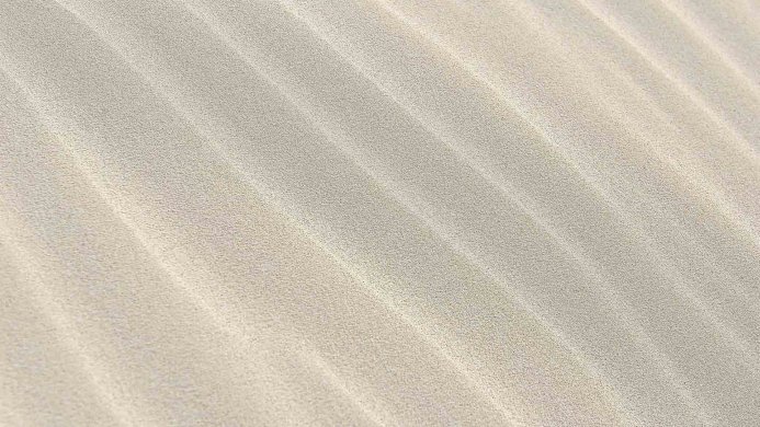 A close-up view of sand with wave-like patterns created by wind or water