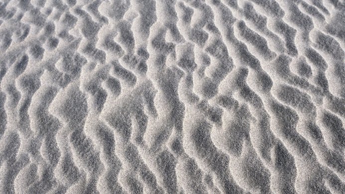 Close-up of sand ripples creating a textured pattern in shades of gray and white