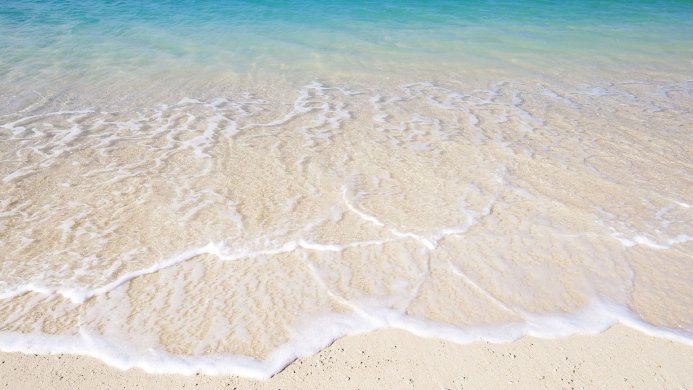 Waves gently lapping onto a sandy beach with clear turquoise water