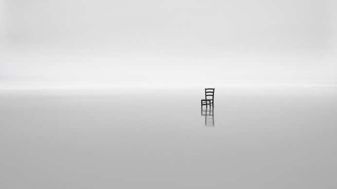 A single chair in a vast, empty, monochrome space, reflecting on the surface