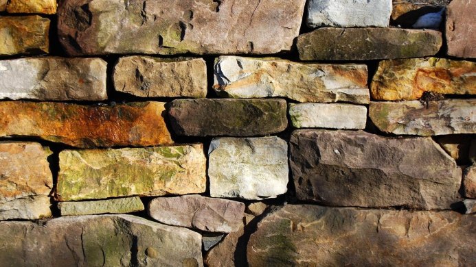 A stone wall constructed of uneven shaped brown, gray, and green stones