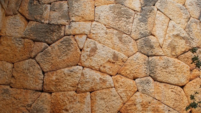 A wall made of irregularly shaped, rough-textured stone blocks in shades of brown, orange, and gray