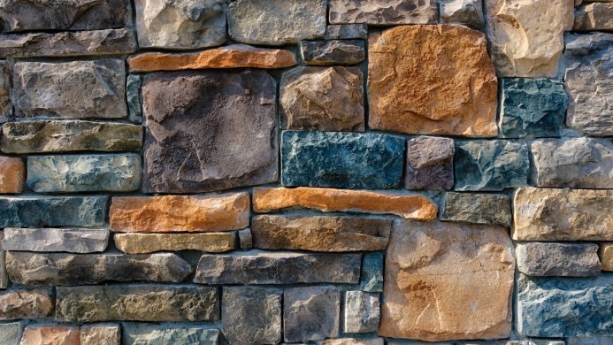 Stone wall with grey, orange, blue and brown stones in an ashlar pattern