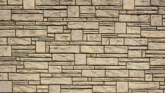 A tan brick wall with varying sized bricks forming a textured pattern