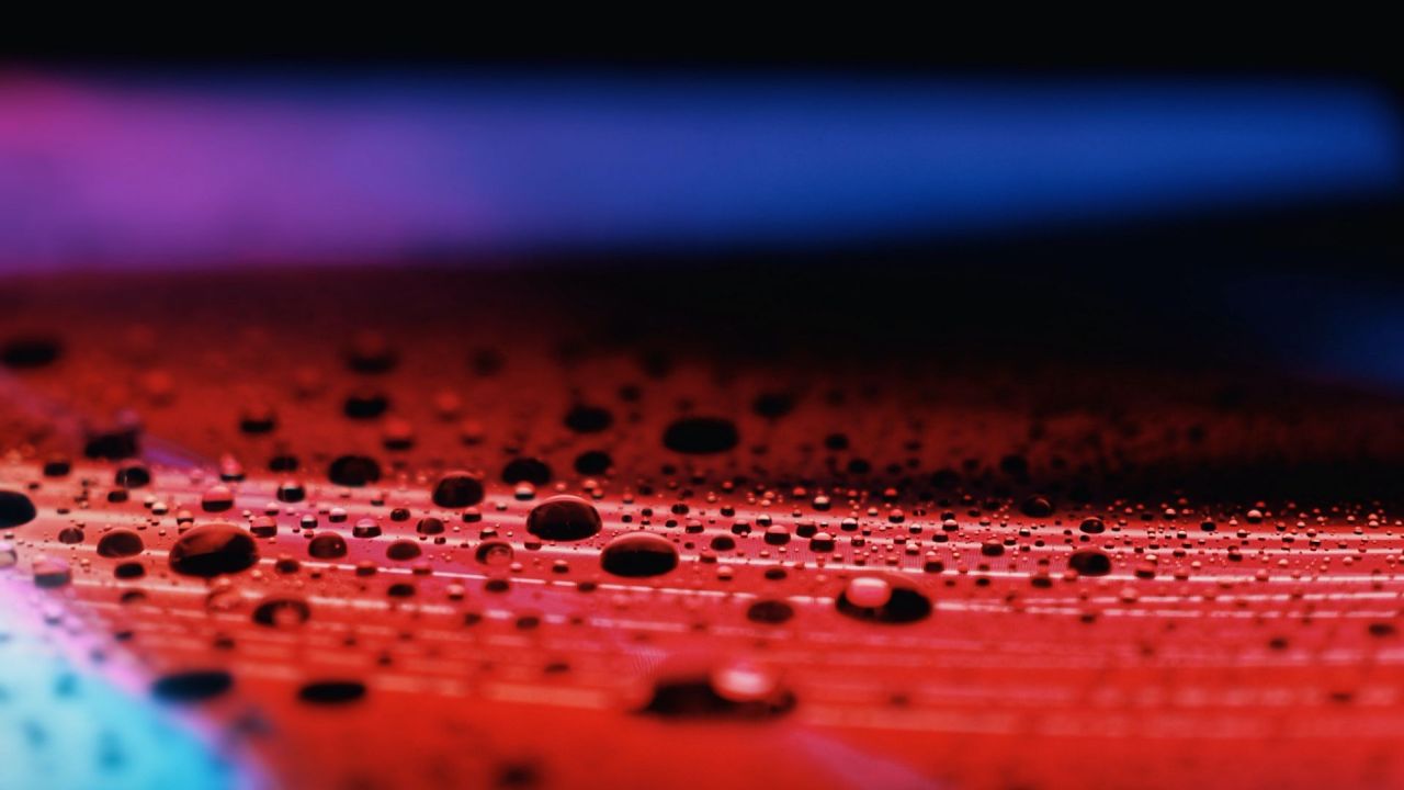 Water droplets on red surface with blue and purple light