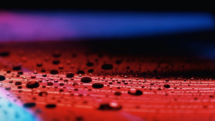 Close-up of water droplets on a red surface with a blue and purple background